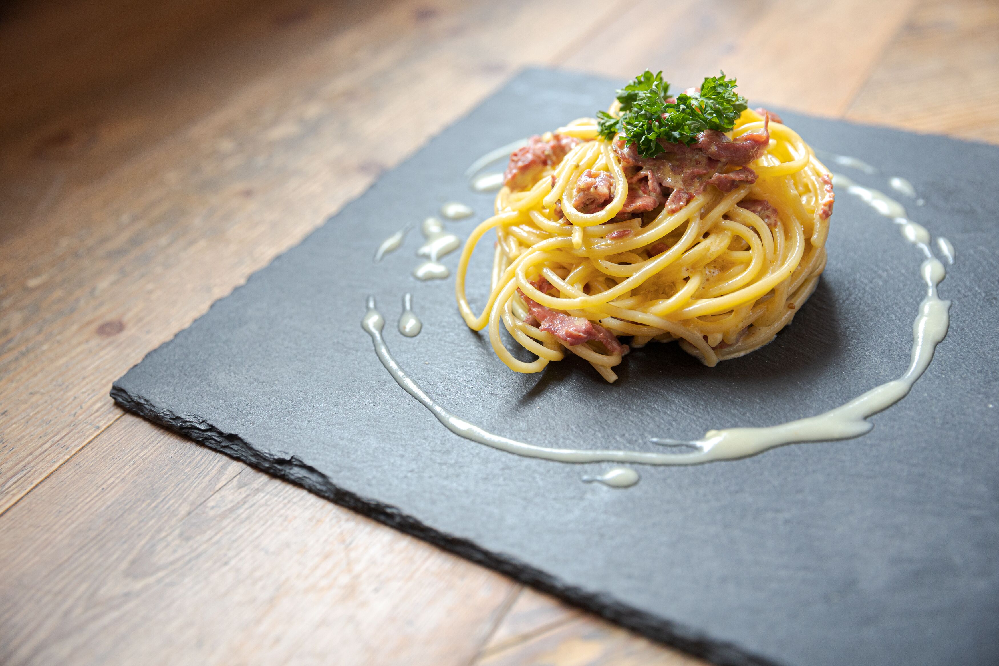 A plate of spaghetti with meat and a garnish on a slate serving board.