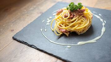 A plate of spaghetti with meat and a garnish on a slate serving board.