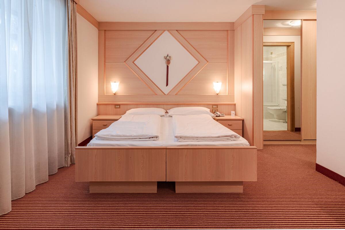 A hotel room with a large bed, wooden headboard, two bedside tables, a nightstand, a mirror, and a red carpeted floor.