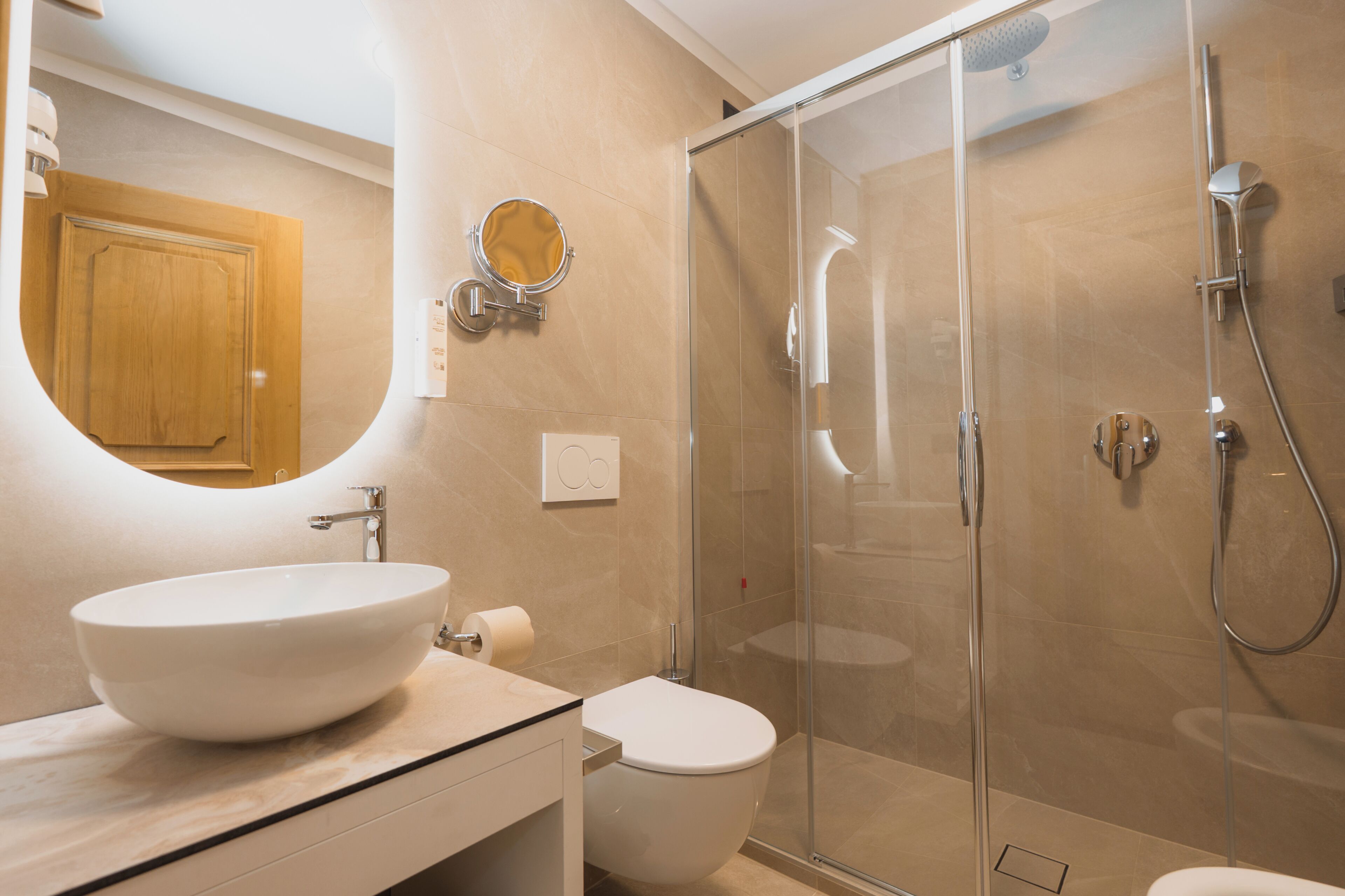 A modern bathroom with a large oval sink, a toilet, a glass-enclosed shower, and a wooden cabinet in the background.
