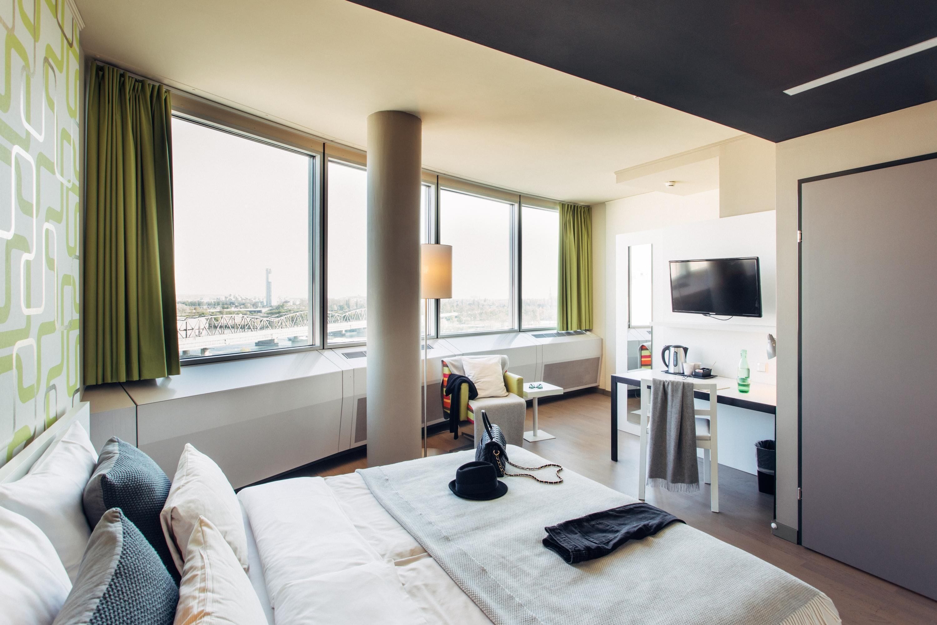 Habitació d'hotel amb llit, escriptori, cadira, televisió i finestra amb vista a la ciutat.