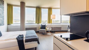 Ein Hotelzimmer mit Bett, Schreibtisch, Stuhl, Lampe und Blick auf die Stadt.