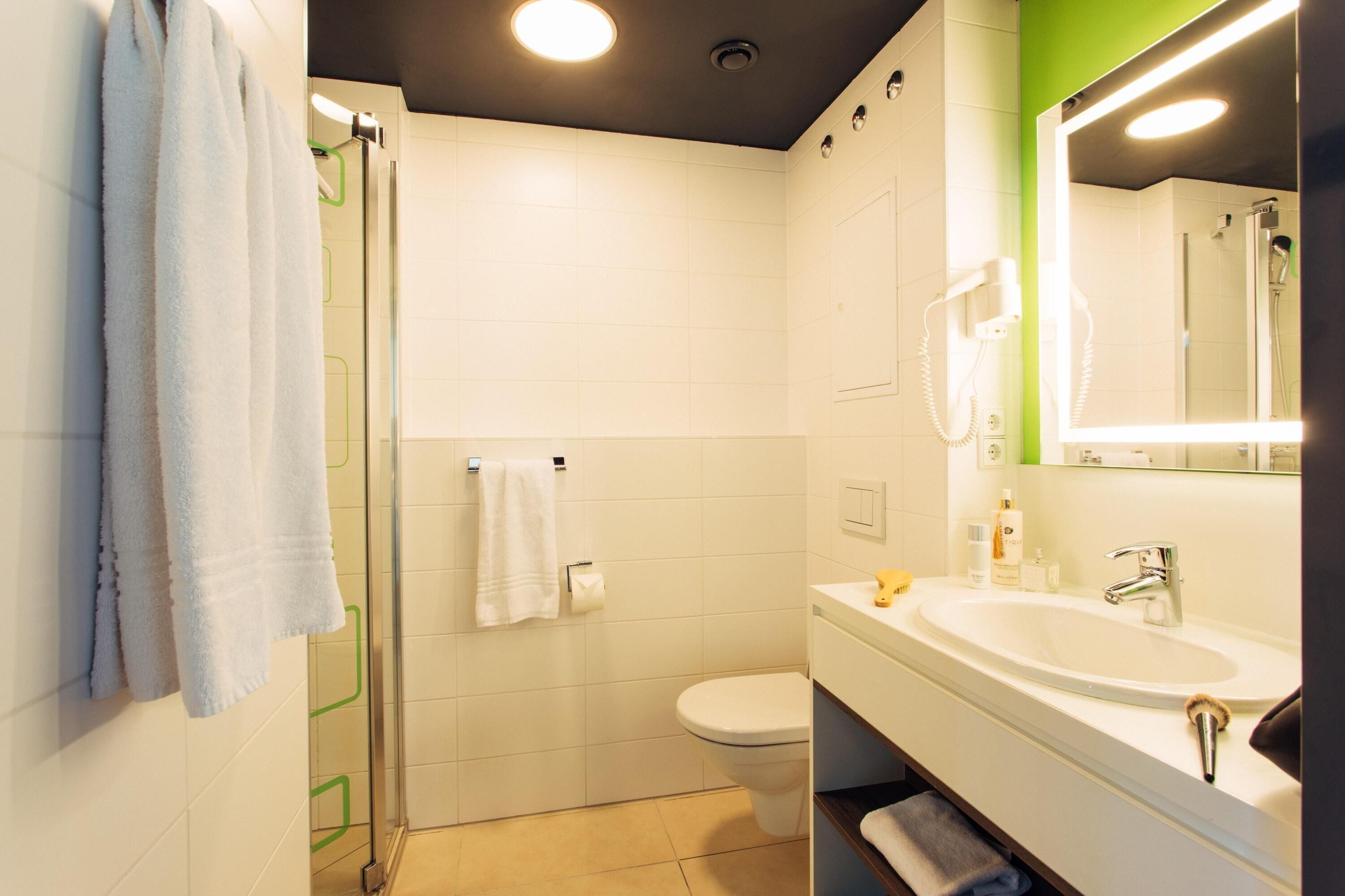 Un baño moderno con cabina de ducha de vidrio, un inodoro blanco y un tocador con espejo.