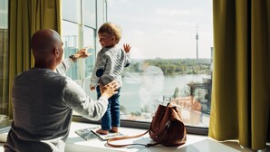 Ein Zimmer mit einem großen Fenster mit Blick auf eine Stadtlandschaft, ein Tisch mit einem Laptop und eine Handtasche auf der Fensterbank.