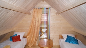 Une petite chambre mansardée, chaleureuse et accueillante, avec deux lits simples, une table en bois et une grande fenêtre avec un rideau.