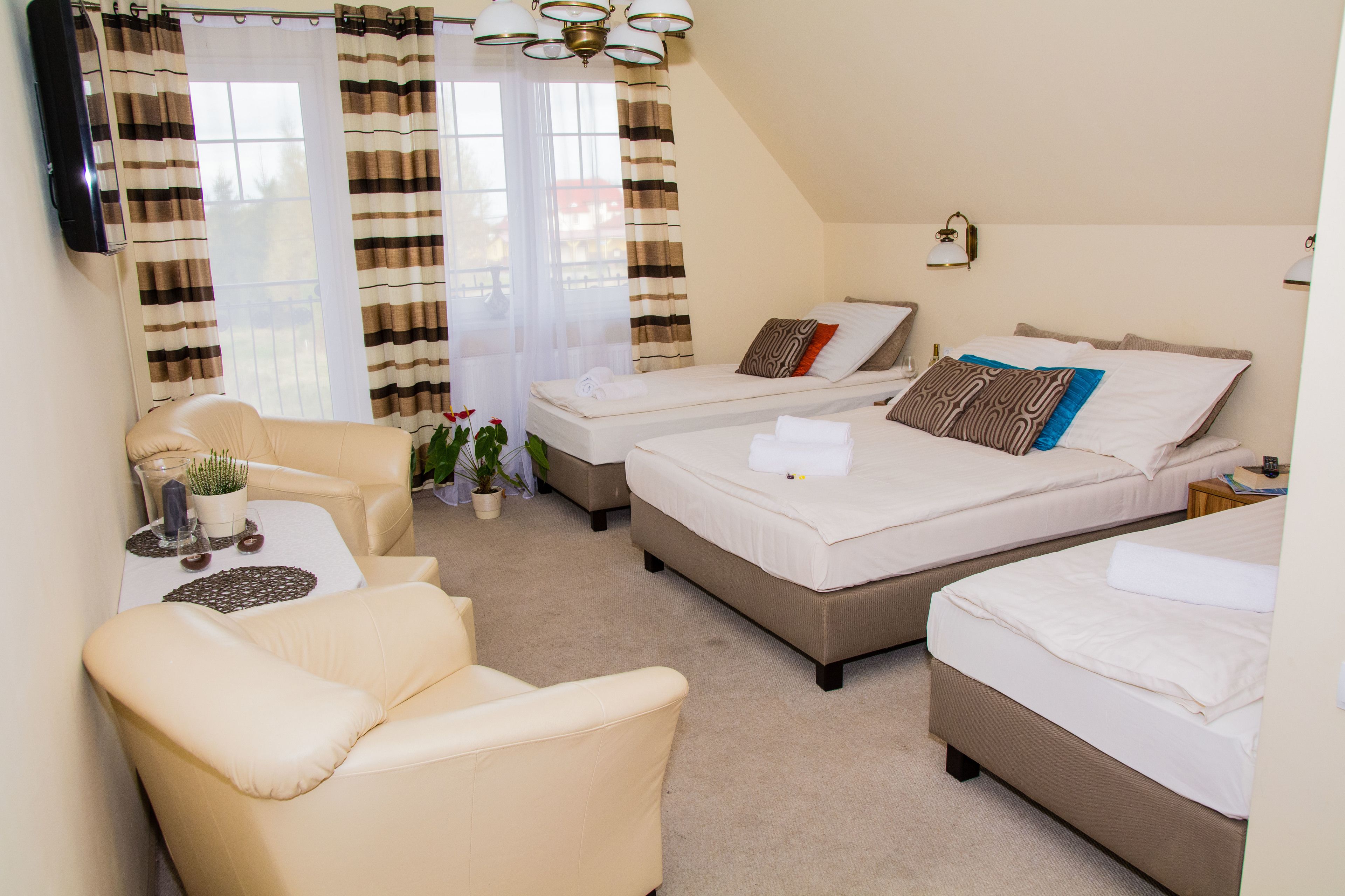 A hotel room with two beds, a sofa, a small table with a plant, and a TV mounted on the wall.