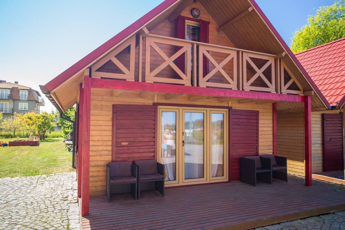 Una cabaña de madera con terraza cubierta, puertas correderas de vidrio grandes y mobiliario exterior.