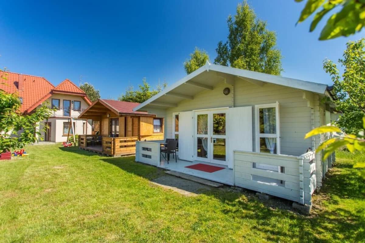 Una cabaña de estilo blanco con techo rojo, un porche con un felpudo rojo y una pequeña terraza.