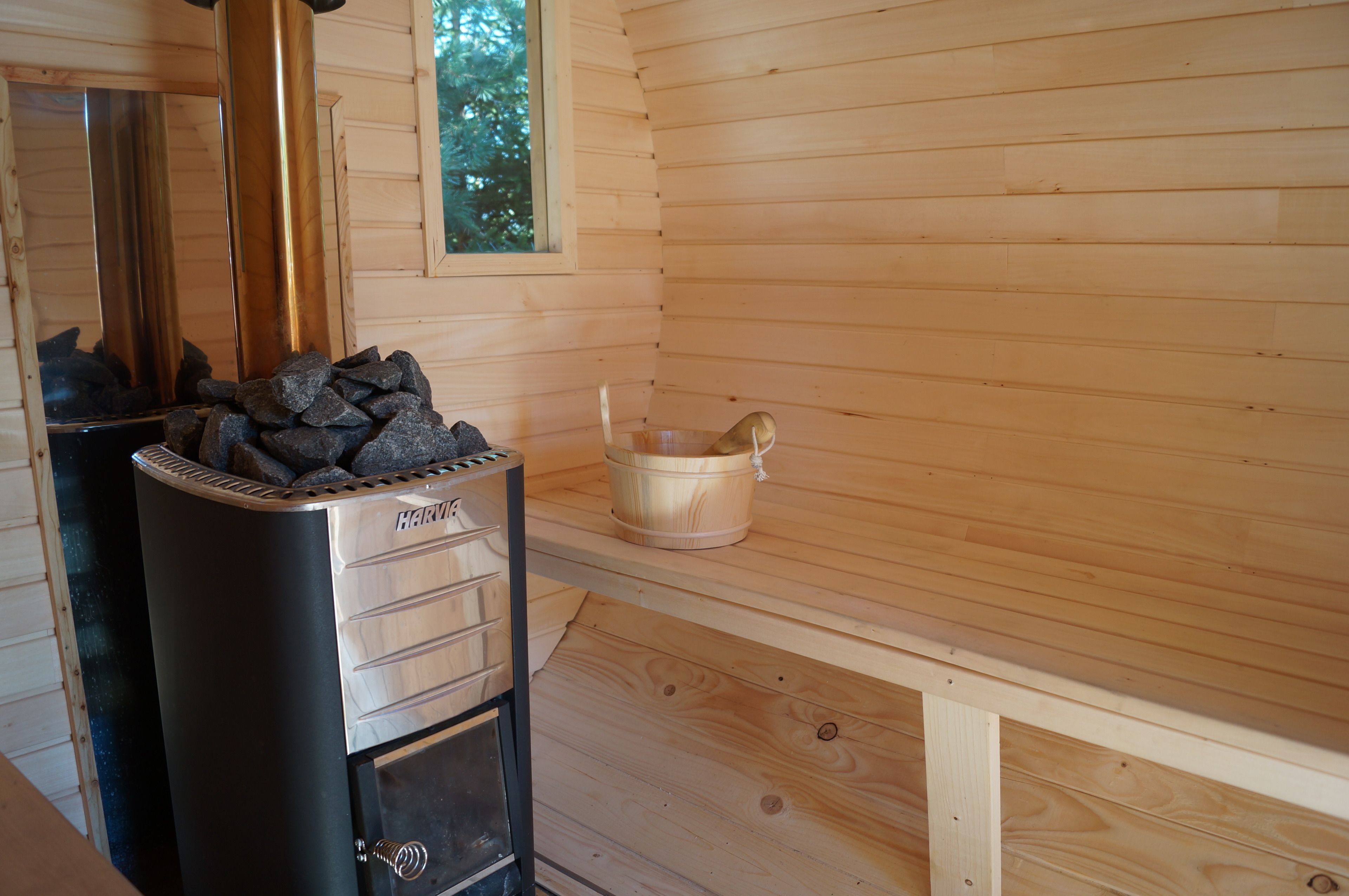 A sauna room with a sauna heater, a wooden bench, and a bucket.