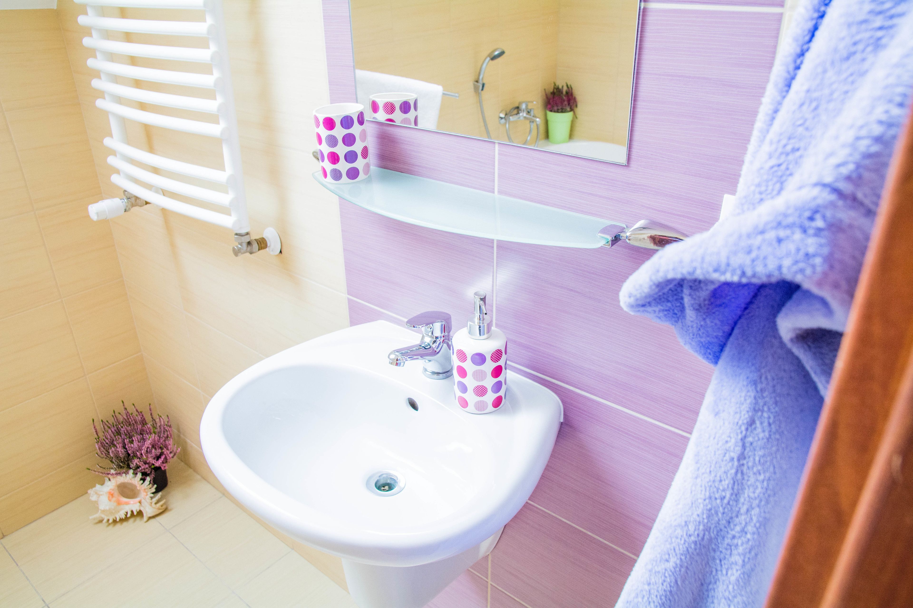 Un baño con lavamanos blanco, un espejo, una toalla y una estantería con una taza rosa con lunares.
