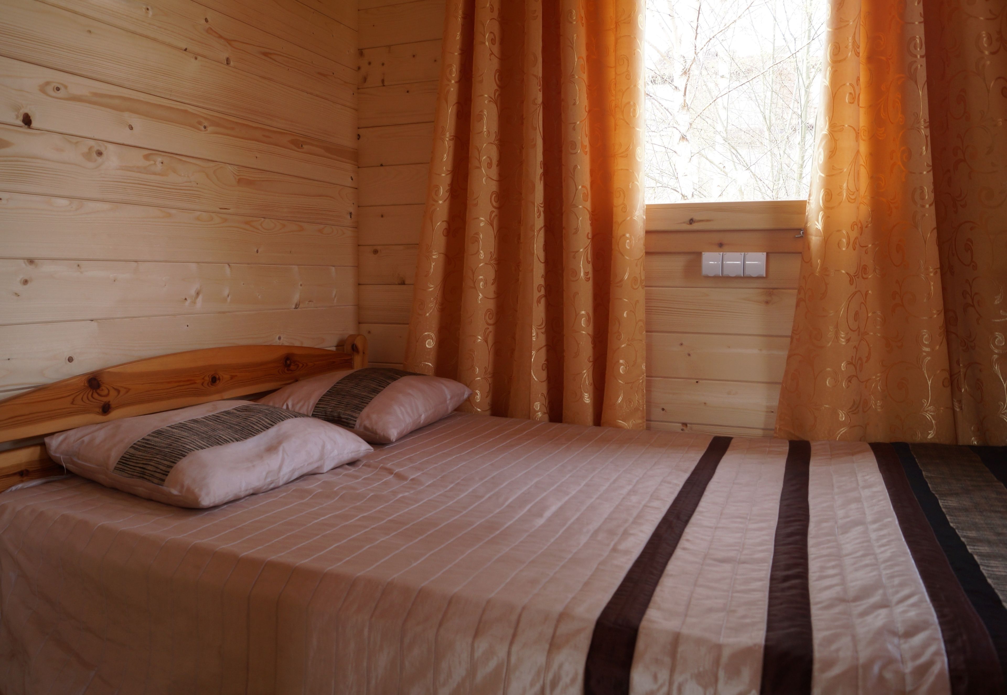 Un dormitorio de cabaña de madera con cama, dos almohadas y cortinas.