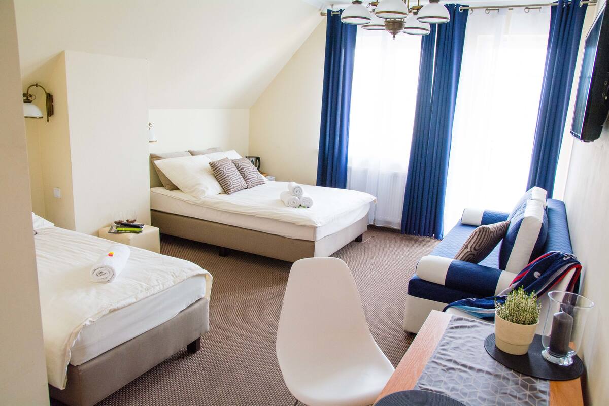 Habitación de hotel con una cama, un sofá, una silla y una mesita con una planta y un vaso.