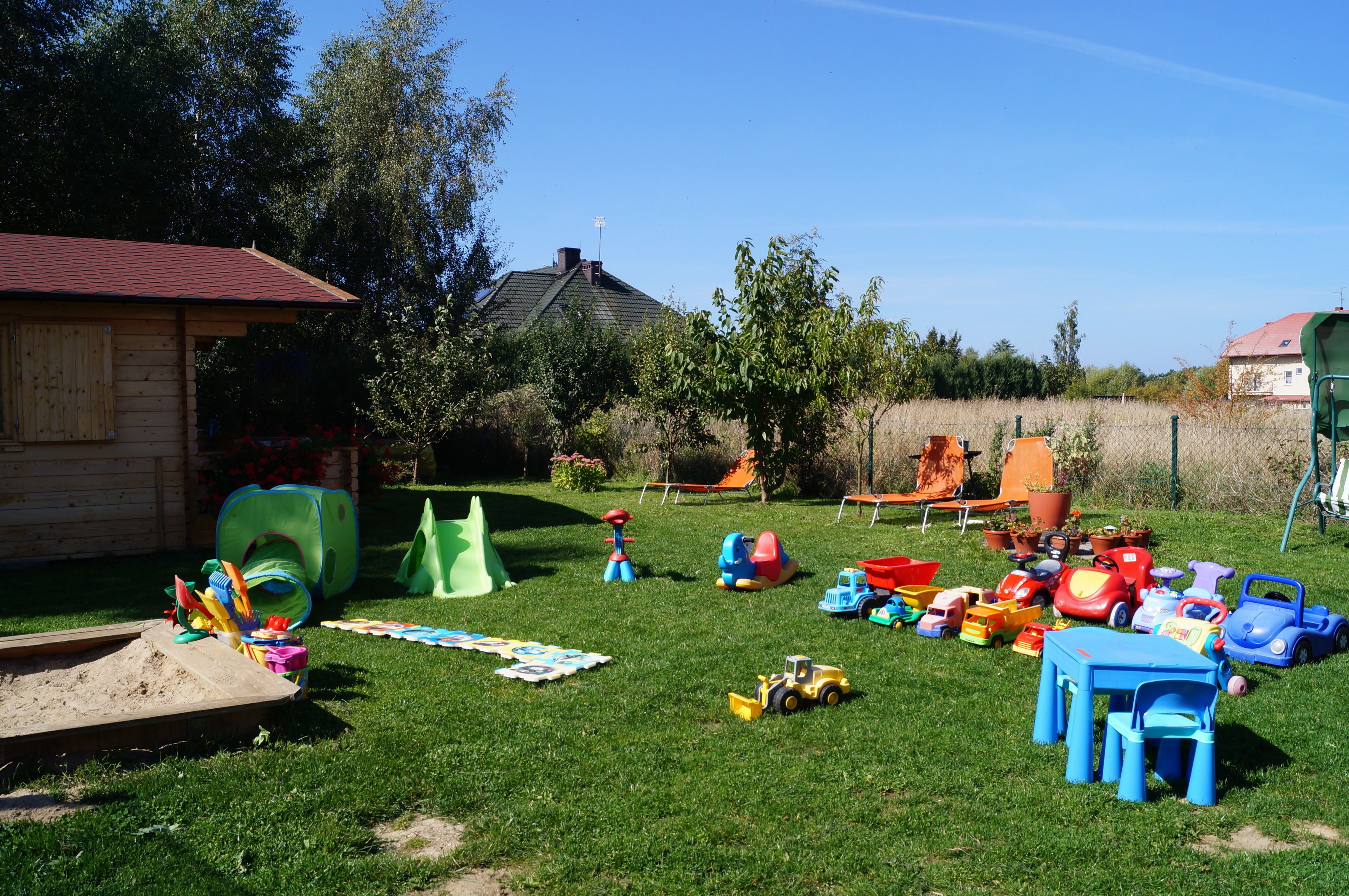 A backyard with a wooden playhouse, a green slide, and various toys and play equipment.