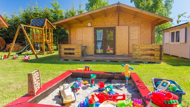Une cabane en bois avec une terrasse, une balançoire et un bac à sable rempli de jouets.