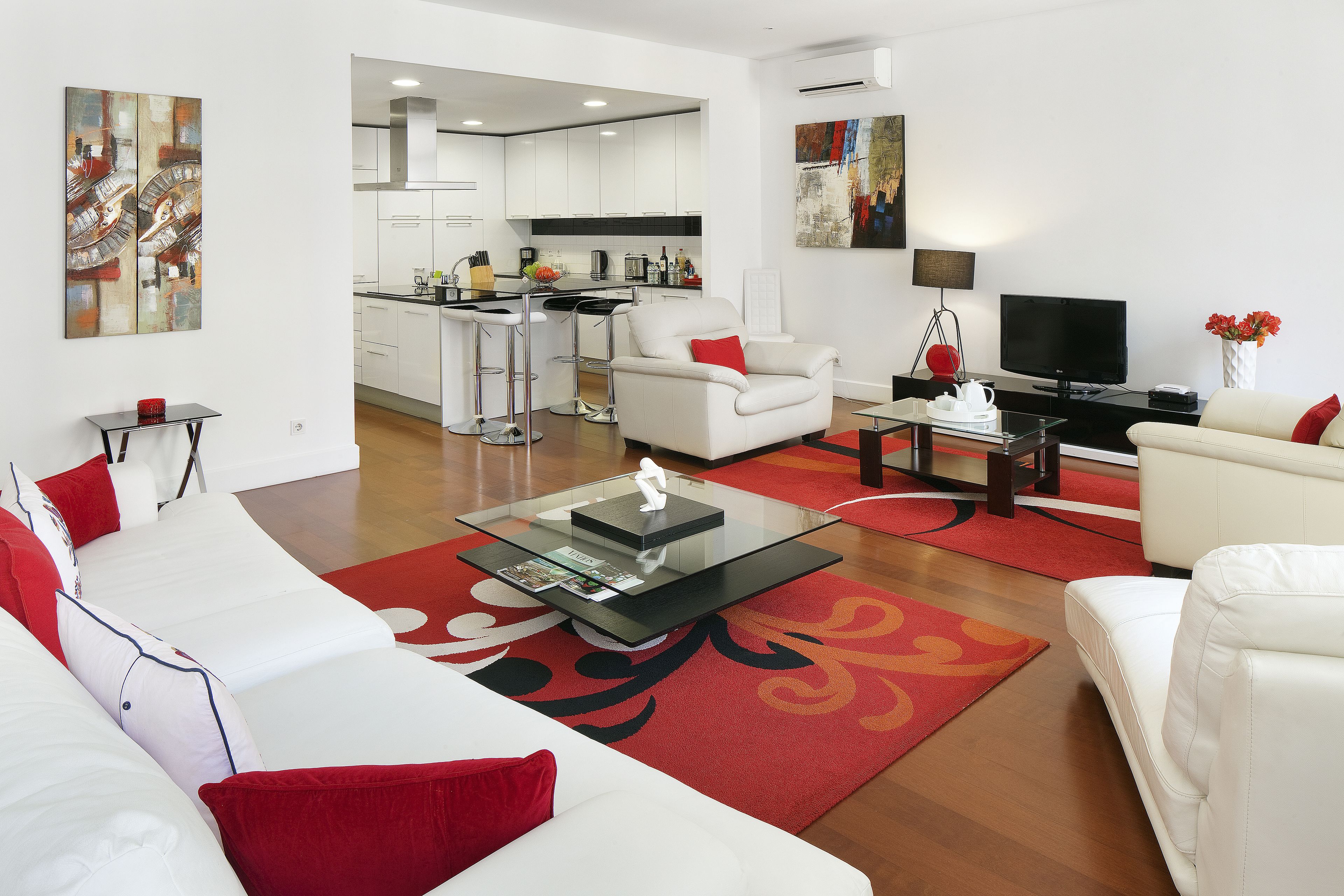 Una sala de estar moderna con un sofá blanco, cojines rojos, una mesa de centro de vidrio y una alfombra roja.