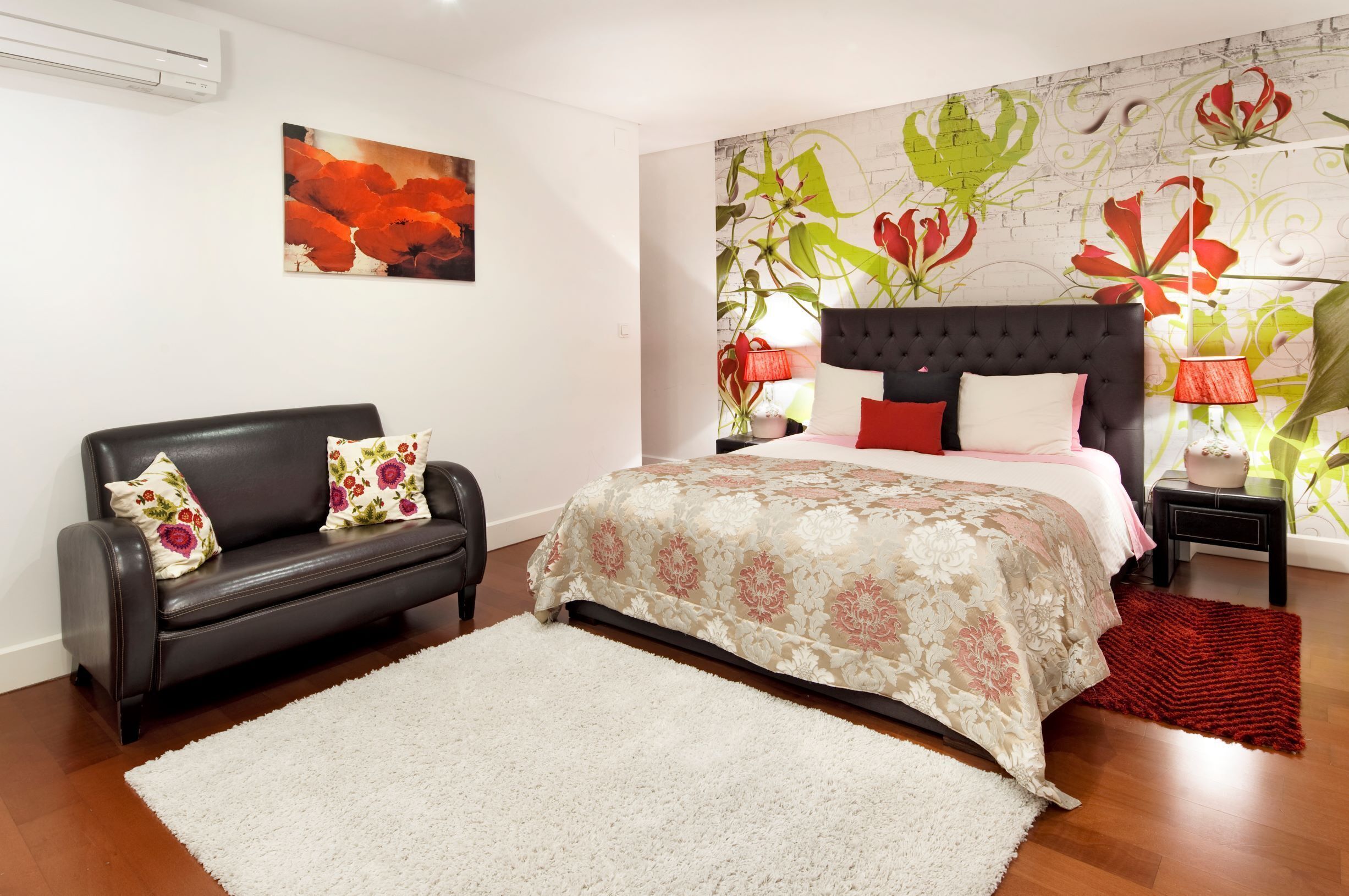 A bedroom with a bed, a black leather sofa, and a red rug.