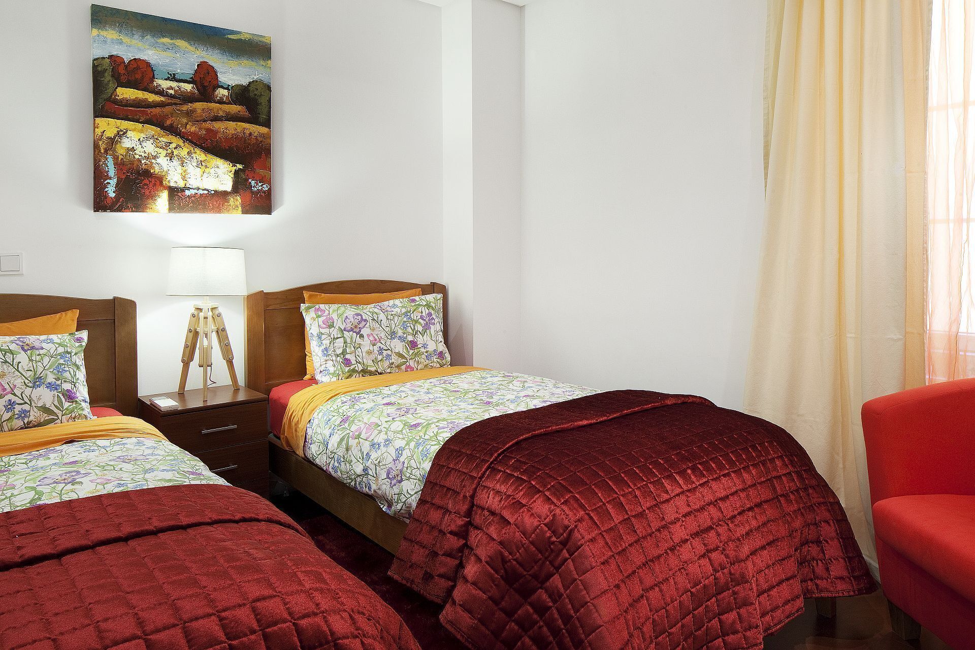 Una habitación de hotel con dos camas, un cuadro en la pared y una silla roja.