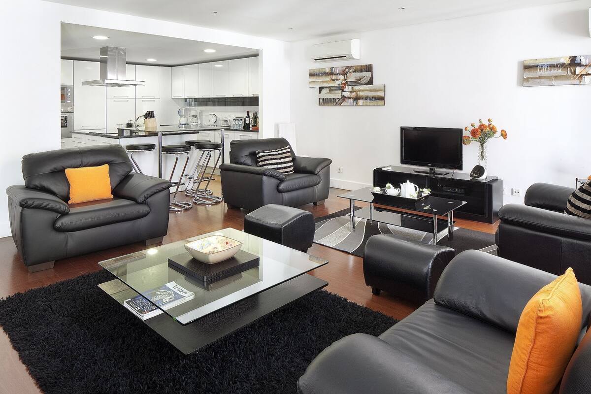 A modern living room with a sofa, armchairs, a coffee table, and a TV.