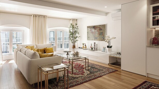 A modern living room with a white sofa, glass coffee table, and a red patterned rug. There is a kitchen area with white cabinets and a refrigerator. - Lisbon Rentals Chiado (Lisbon)