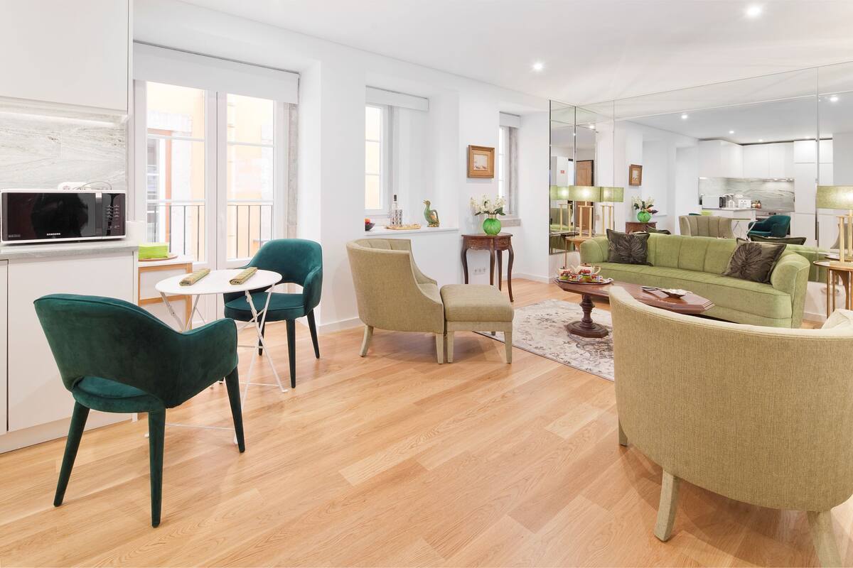 A modern living room with a green sofa, teal chairs, and a wooden floor.
