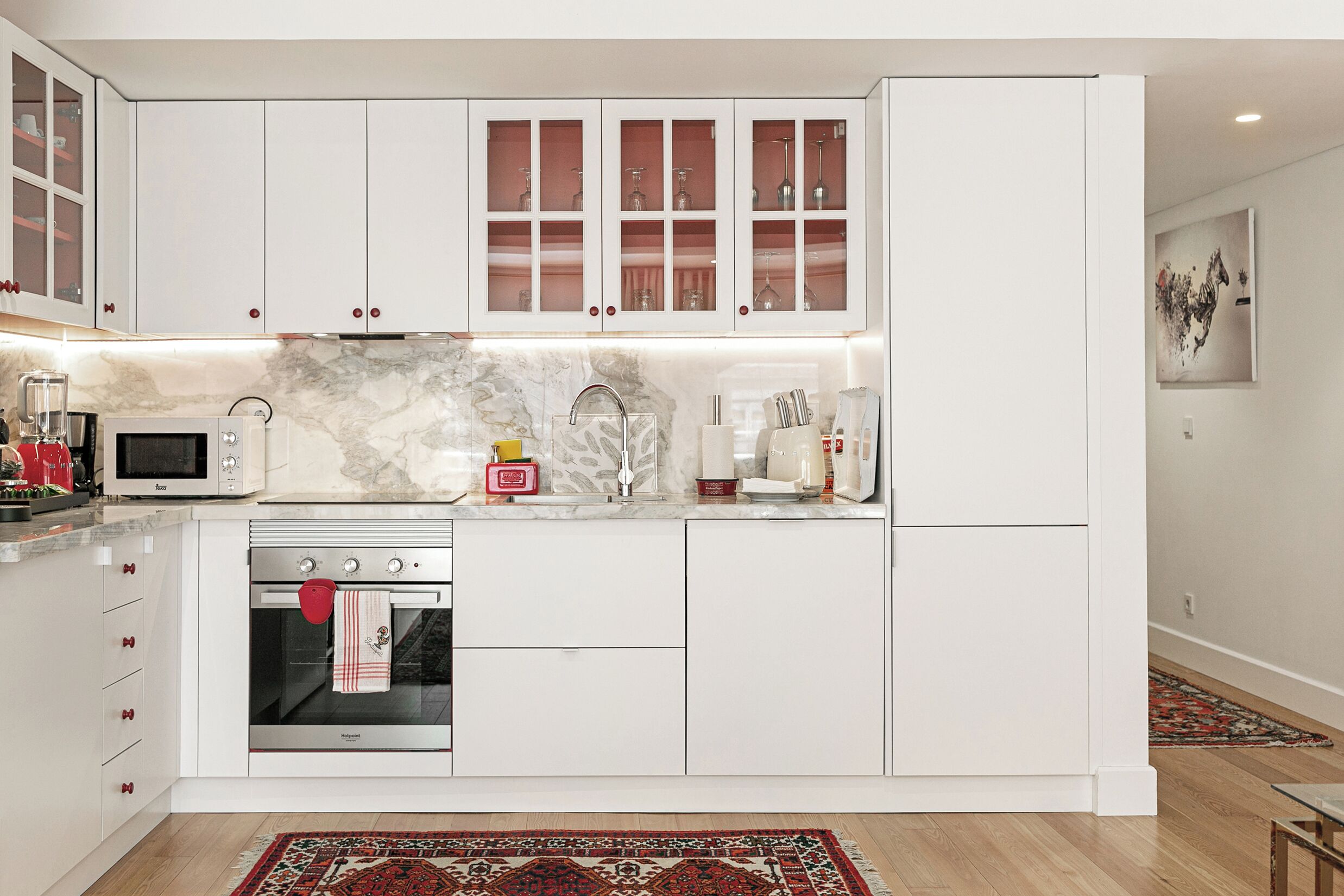 A modern kitchen with white cabinetry, a built-in oven, a microwave, and a marble backsplash.