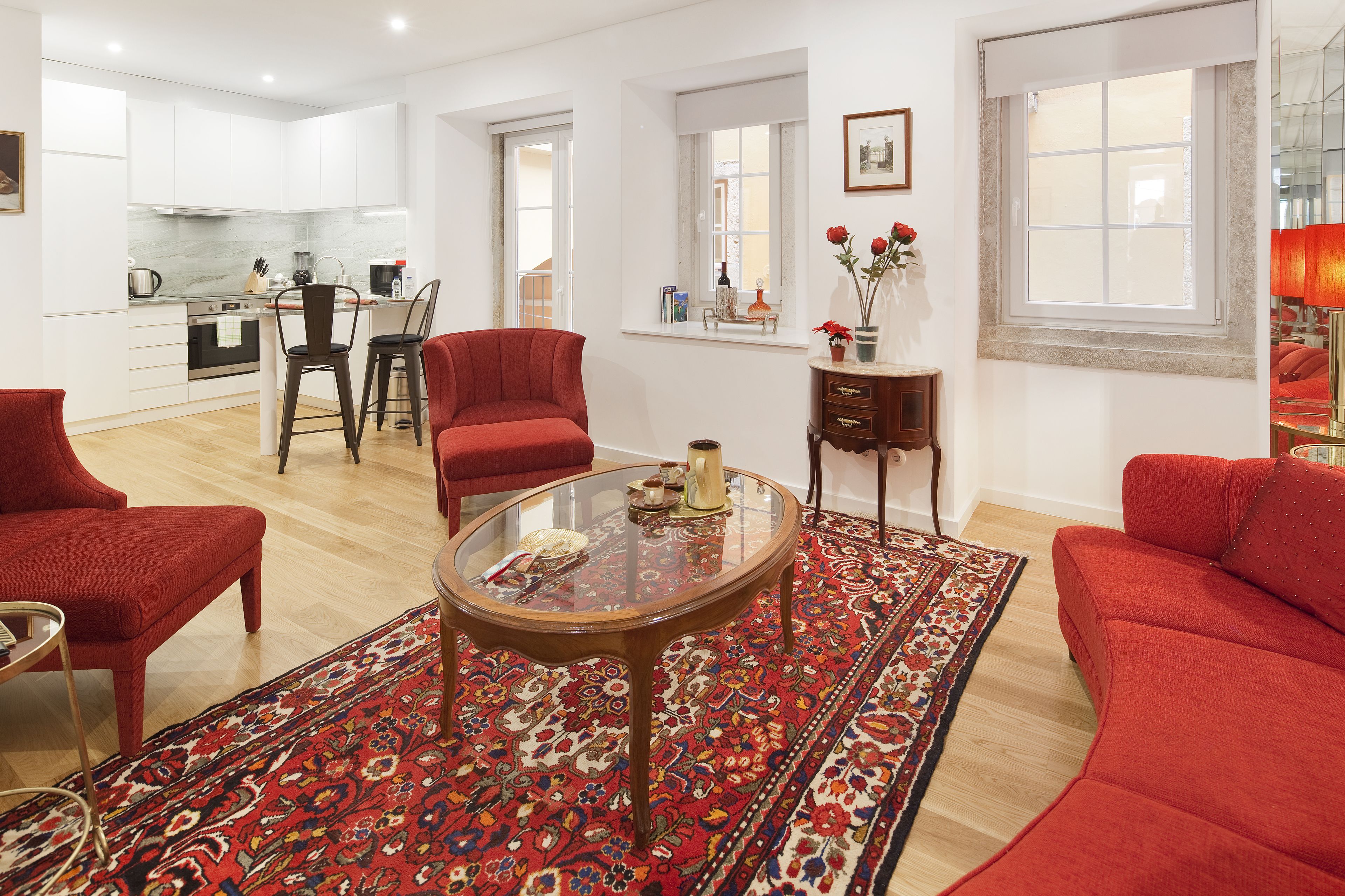 A modern living room with a red sofa, a glass coffee table, and a patterned rug.