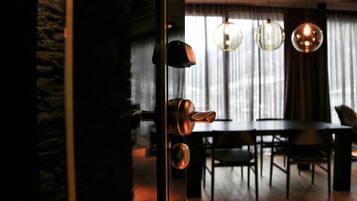 An interior view of a dining area with a wooden table and chairs, a stone wall, and hanging spherical light fixtures.