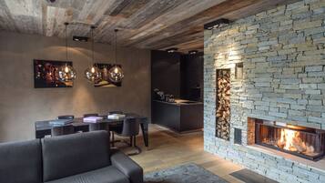 A modern living room with a stone fireplace, a dining area with a table and chairs, and a kitchen in the background.