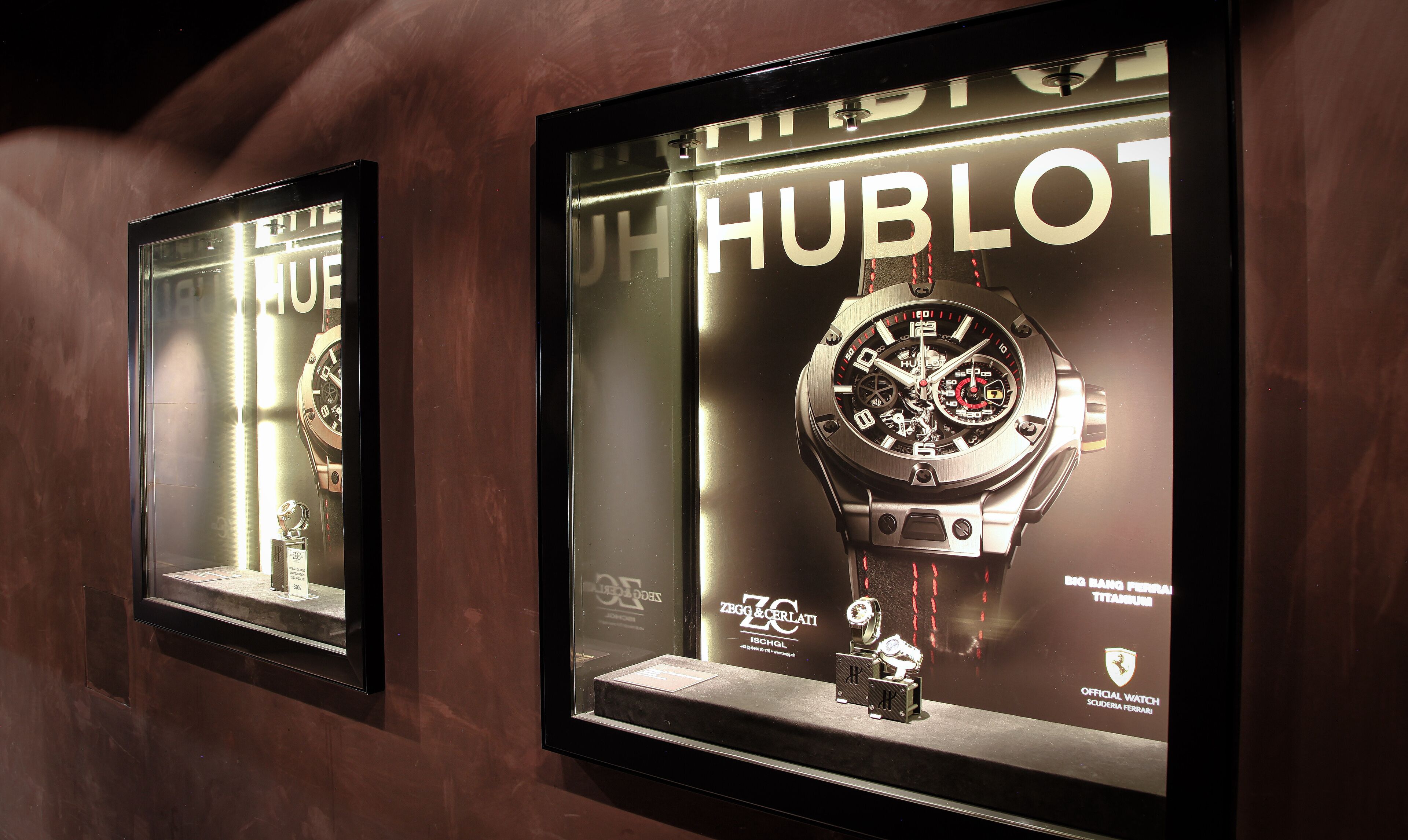 Two framed watch displays with the brand Hublot, showcasing a watch with a large dial and a smaller sub-dial, set against a dark background.