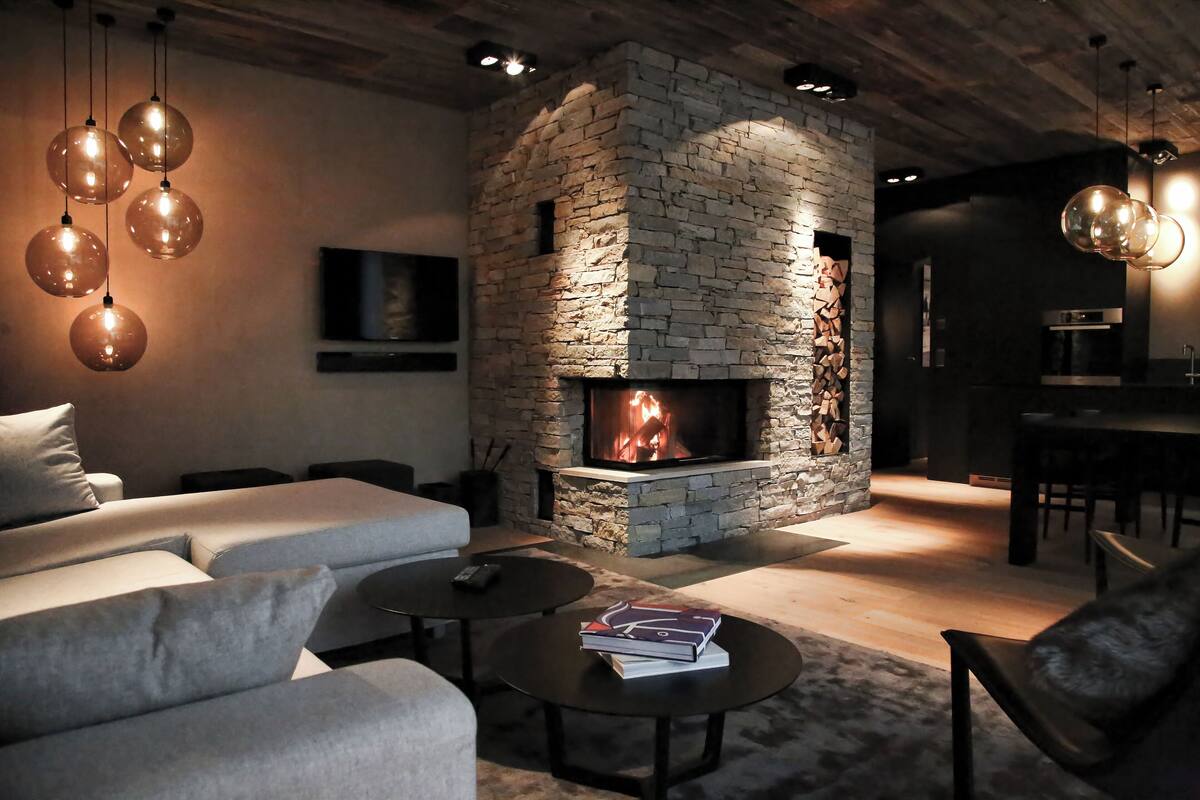 A modern living room with a stone fireplace, sofas, and hanging light fixtures.