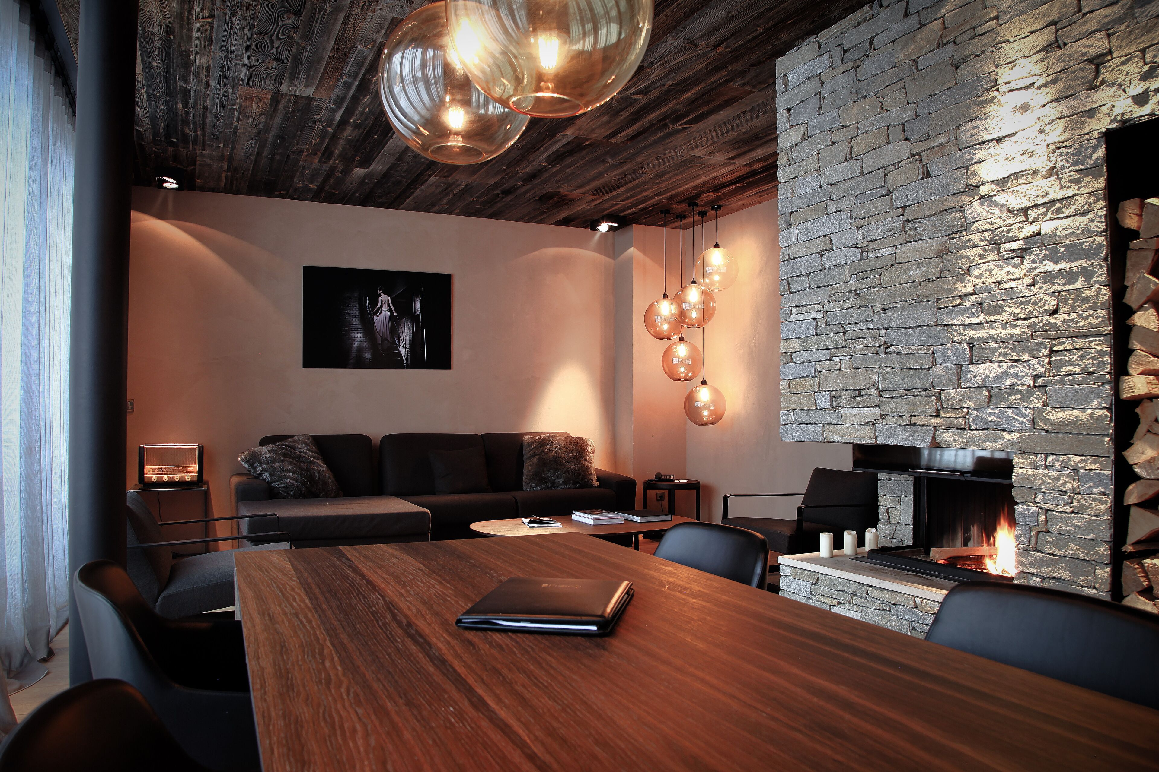 A modern living room with a wooden dining table, a stone fireplace, and a black leather sofa.