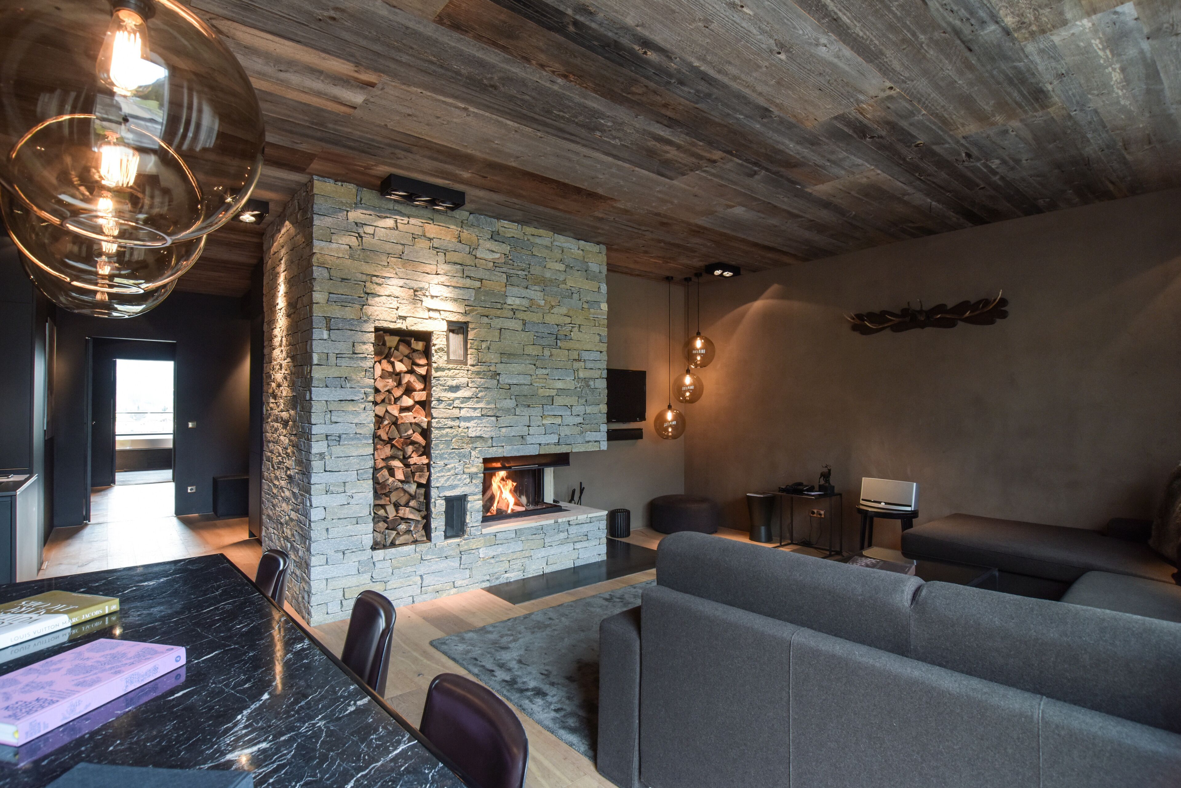 A modern living room with a stone fireplace, a dining area with a marble table, and a cozy seating arrangement.