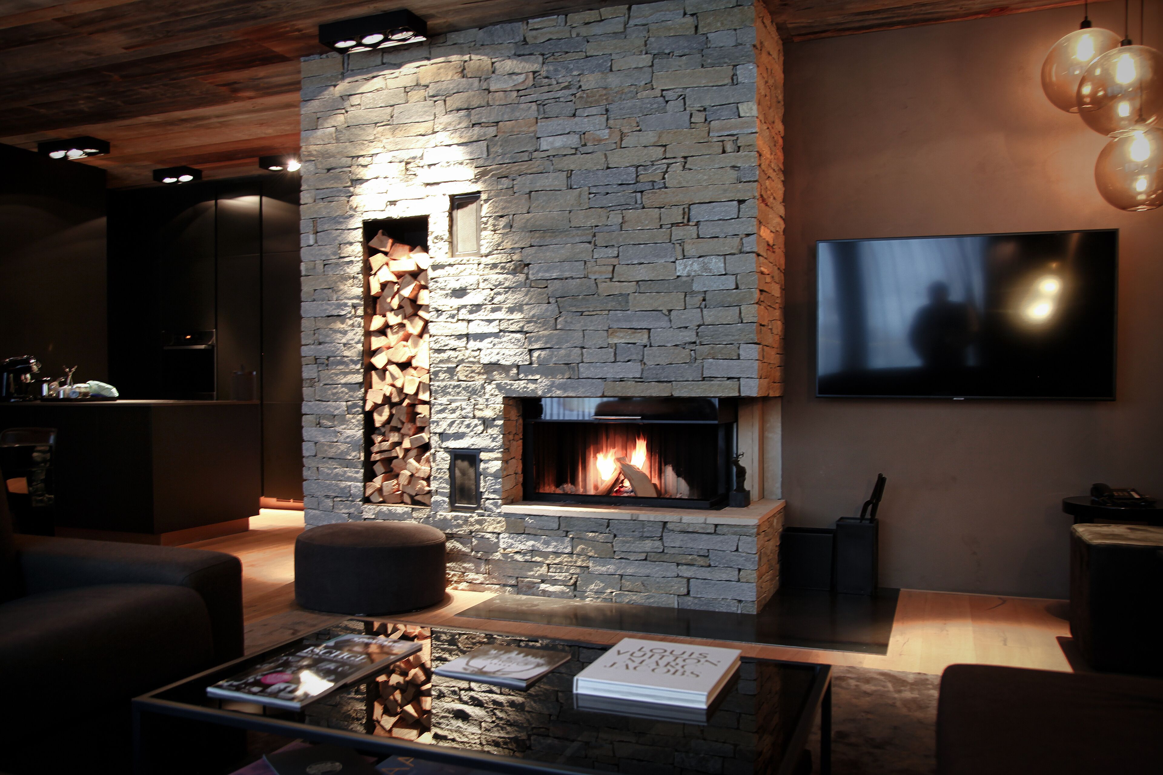 A modern living room with a stone fireplace, a flat-screen TV, and a coffee table with magazines.