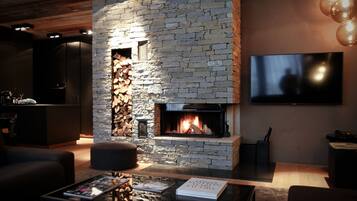 A modern living room with a stone fireplace, a flat-screen TV, and a coffee table with magazines.