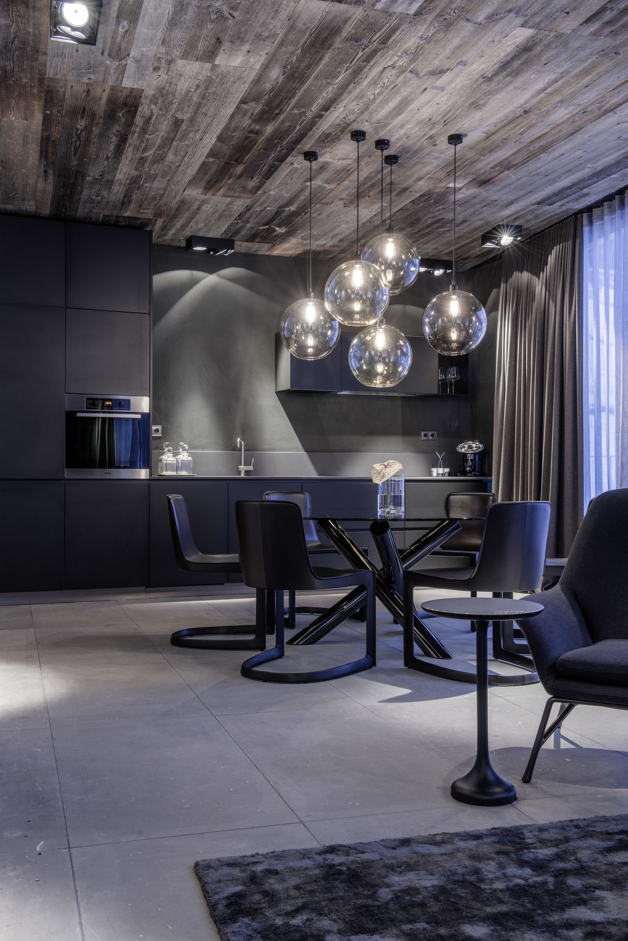 A modern kitchen with a central island, pendant lights, and a dining area with chairs and a table.