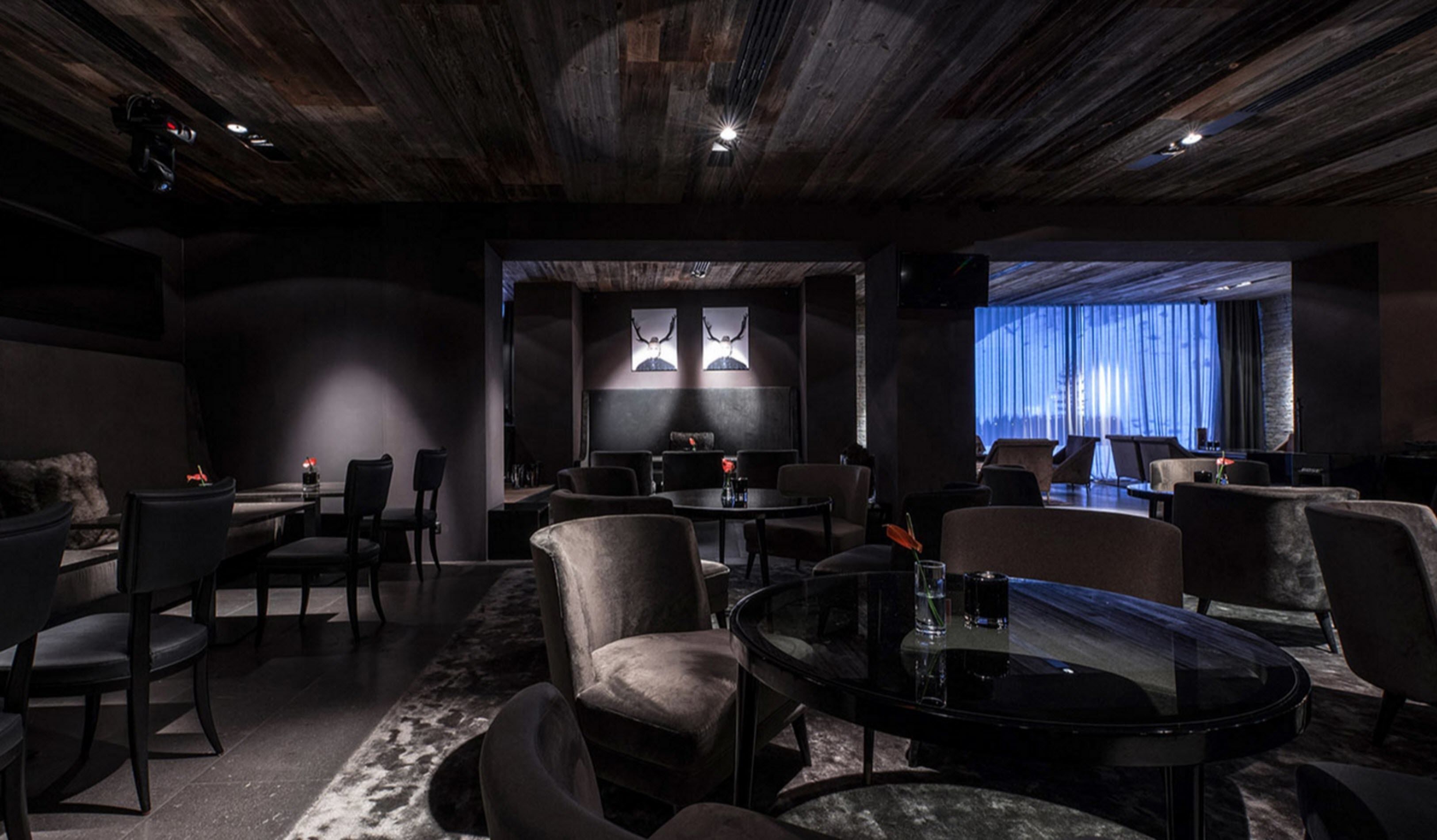 A dimly lit lounge area with a rustic ceiling, round tables, and comfortable seating.