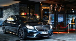 A luxury car parked in front of a building with a red rope barrier, a sign with 'la prairie' and 'GRAND LUXURY' visible, and a large window displaying a snowy landscape. - Hotel Zhero - Ischgl/Kappl (Kappl)