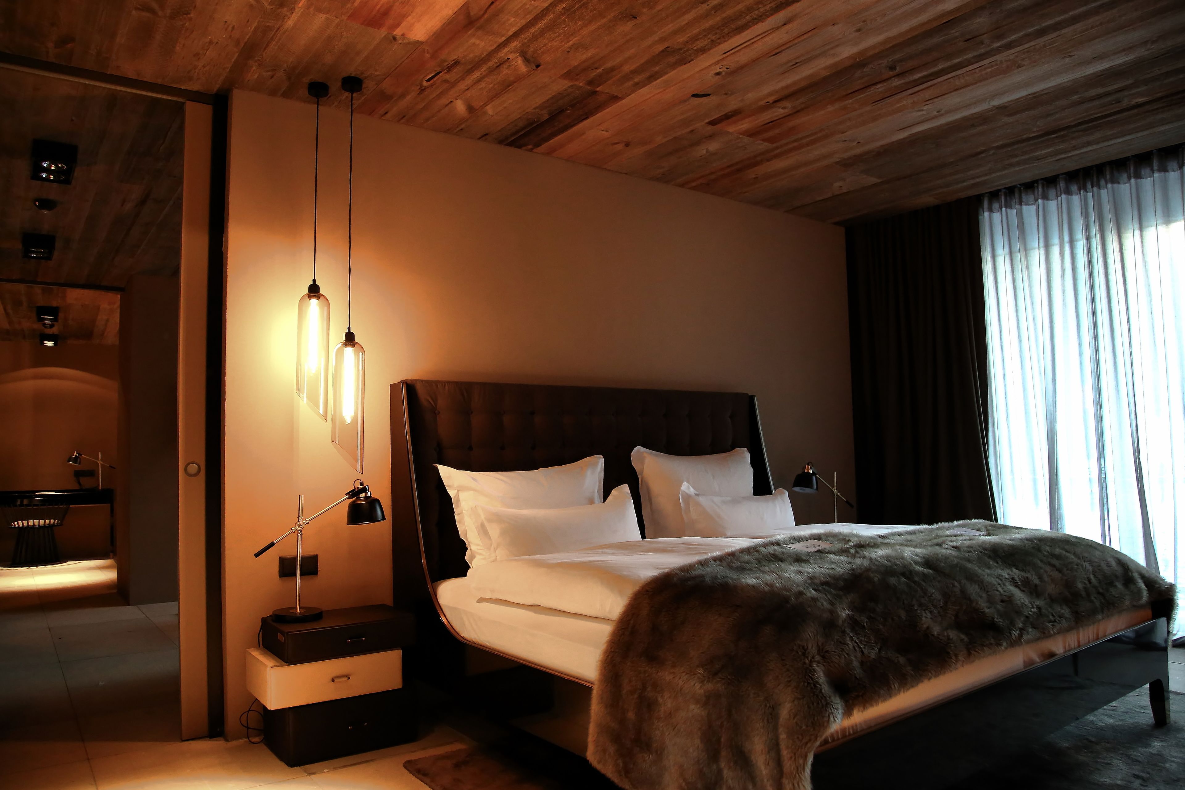 Ein modernes Schlafzimmer mit Holzboden, einem großen Bett mit weißen Leinentüchern, einem Fellüberwurf und Nachttischlampen.