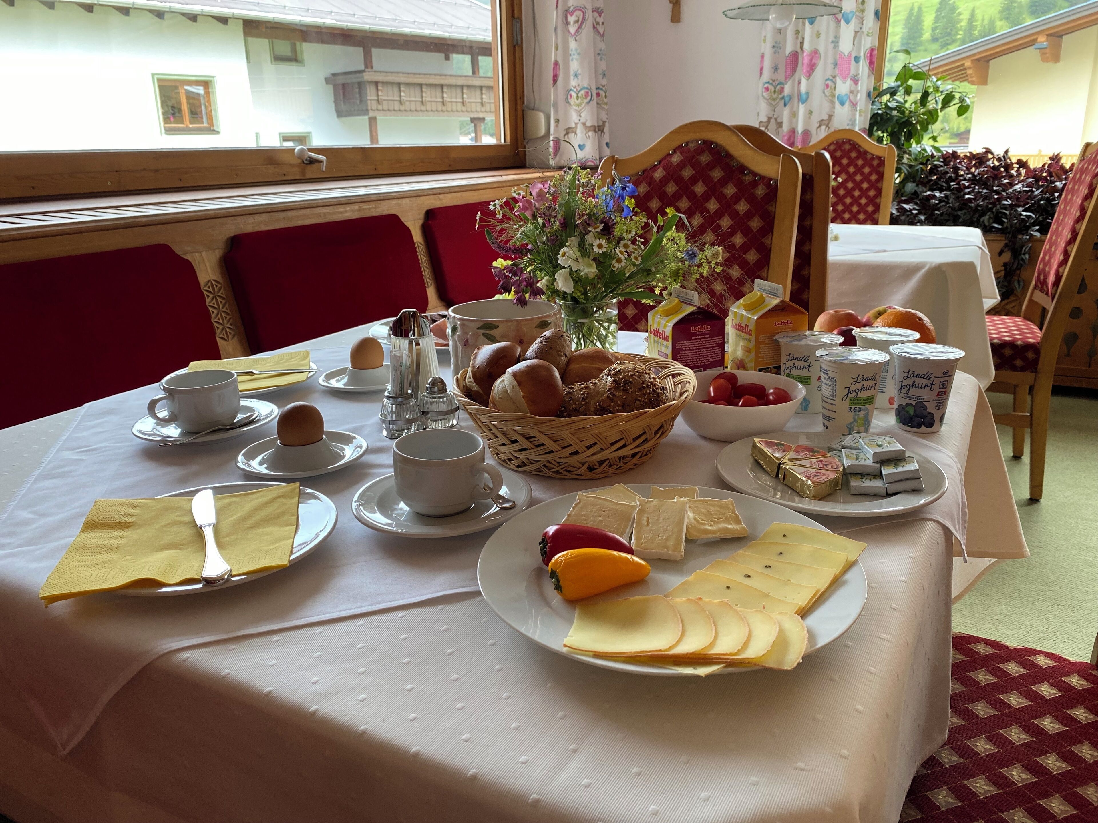 A breakfast table set with plates, cups, bread, butter, cheese, and a fruit bowl.
