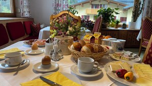 A breakfast table with various food items, including bread, cheese, and eggs, and a vase of flowers. - Haus Schrofenstein (Lech am Arlberg)