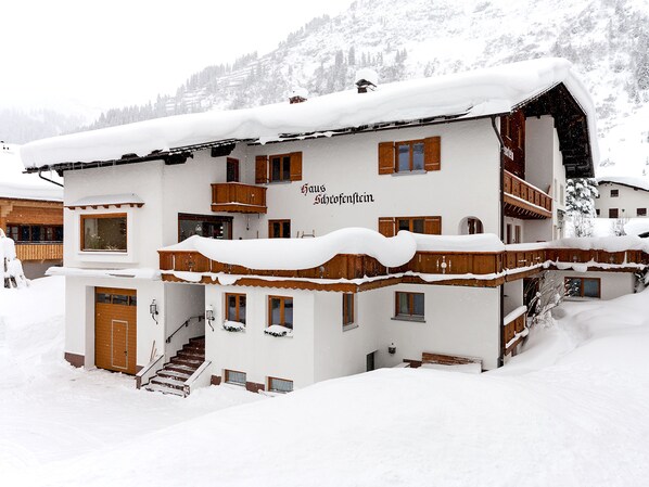 A multi-story building with wooden balconies and a snow-covered roof. - Haus Schrofenstein (Lech am Arlberg)