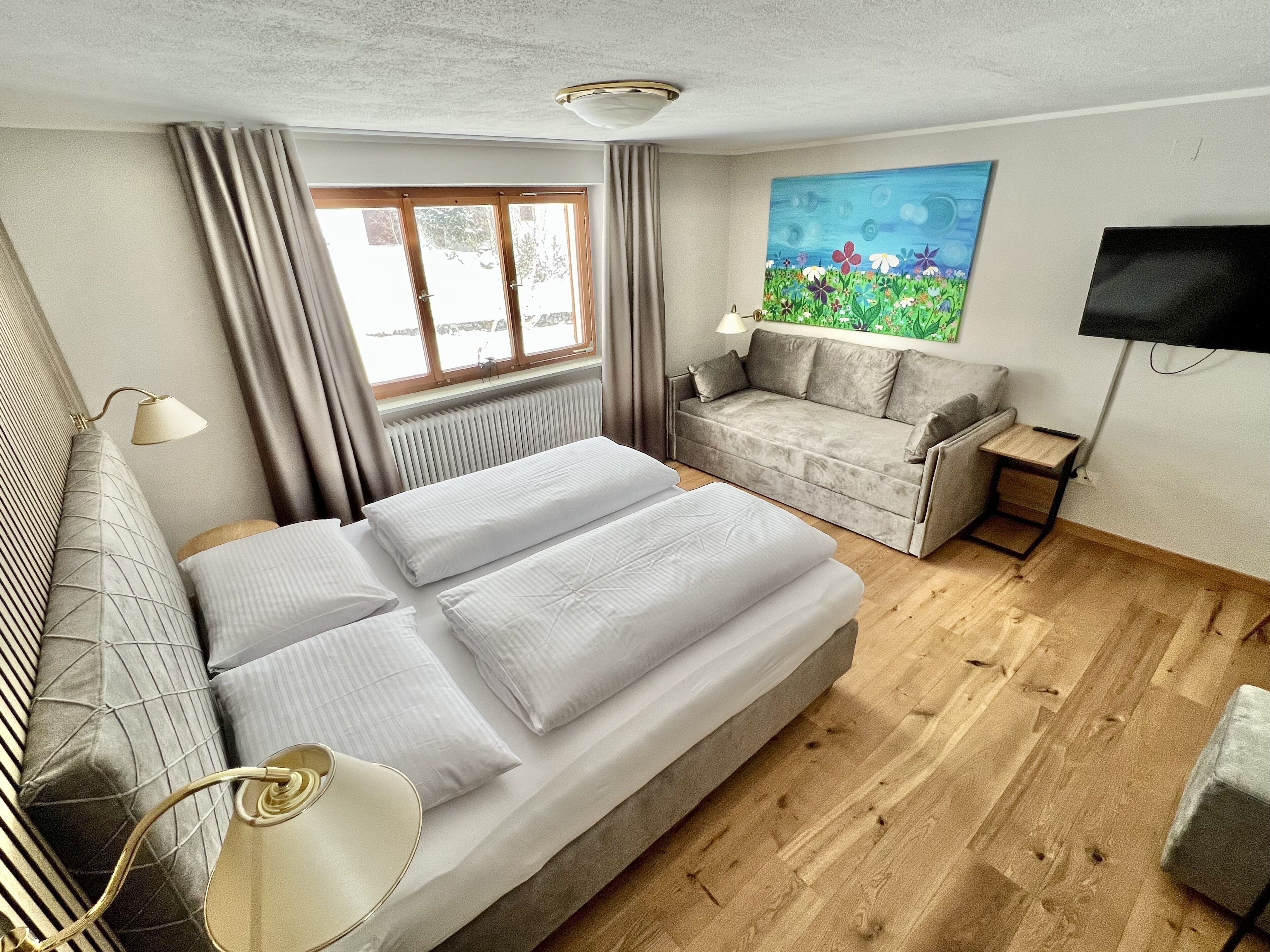 A bedroom with a bed, a sofa, a TV, and a painting.