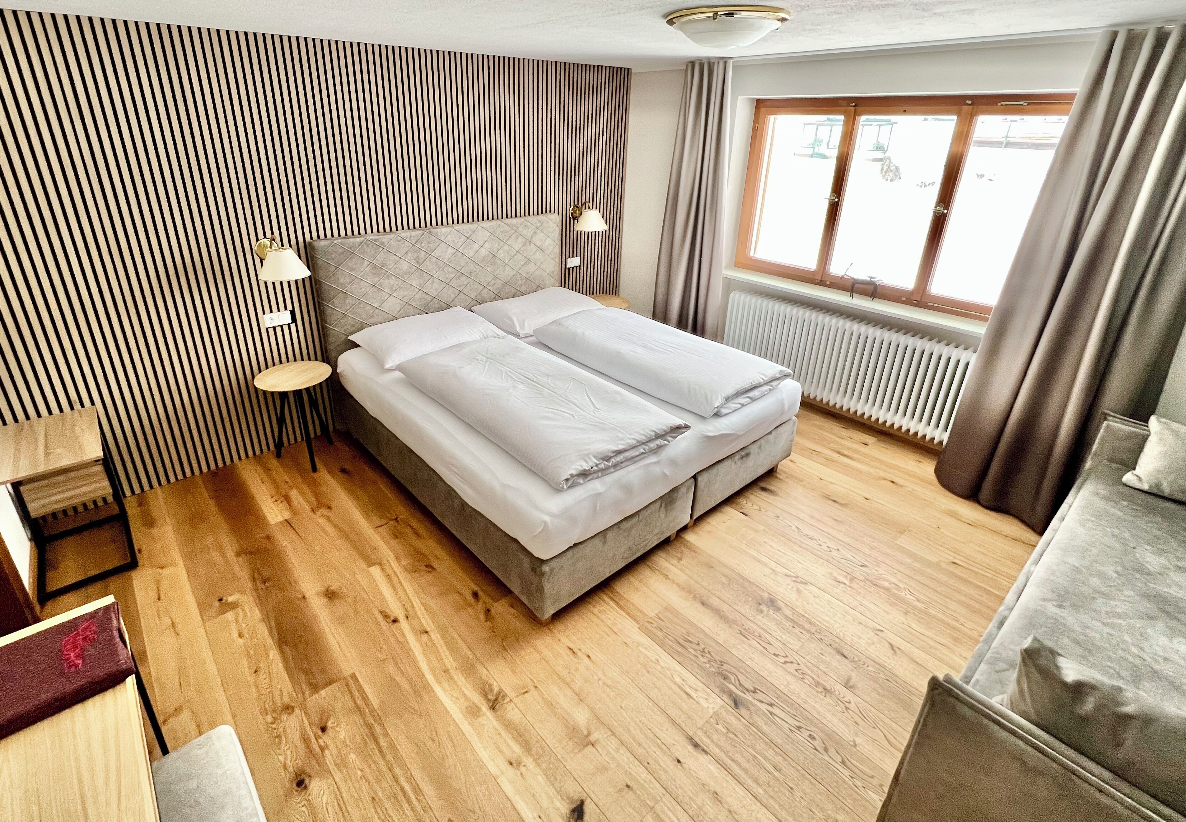 A double bed with a headboard, bedside lamps, a wooden floor, and a window with curtains.
