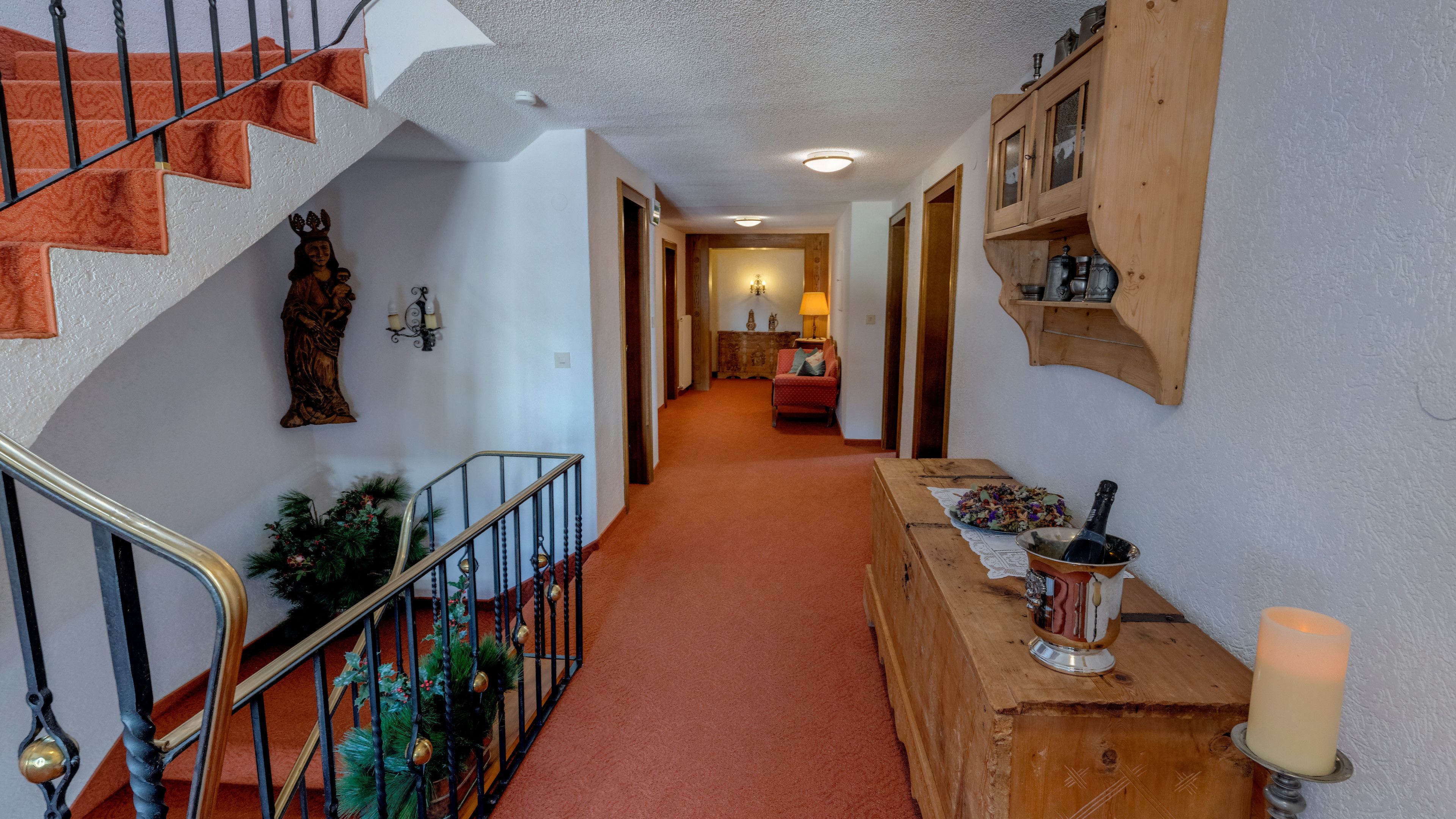 A hallway with a wooden staircase, a wooden cabinet with kitchenware, a candle, and a red chair.