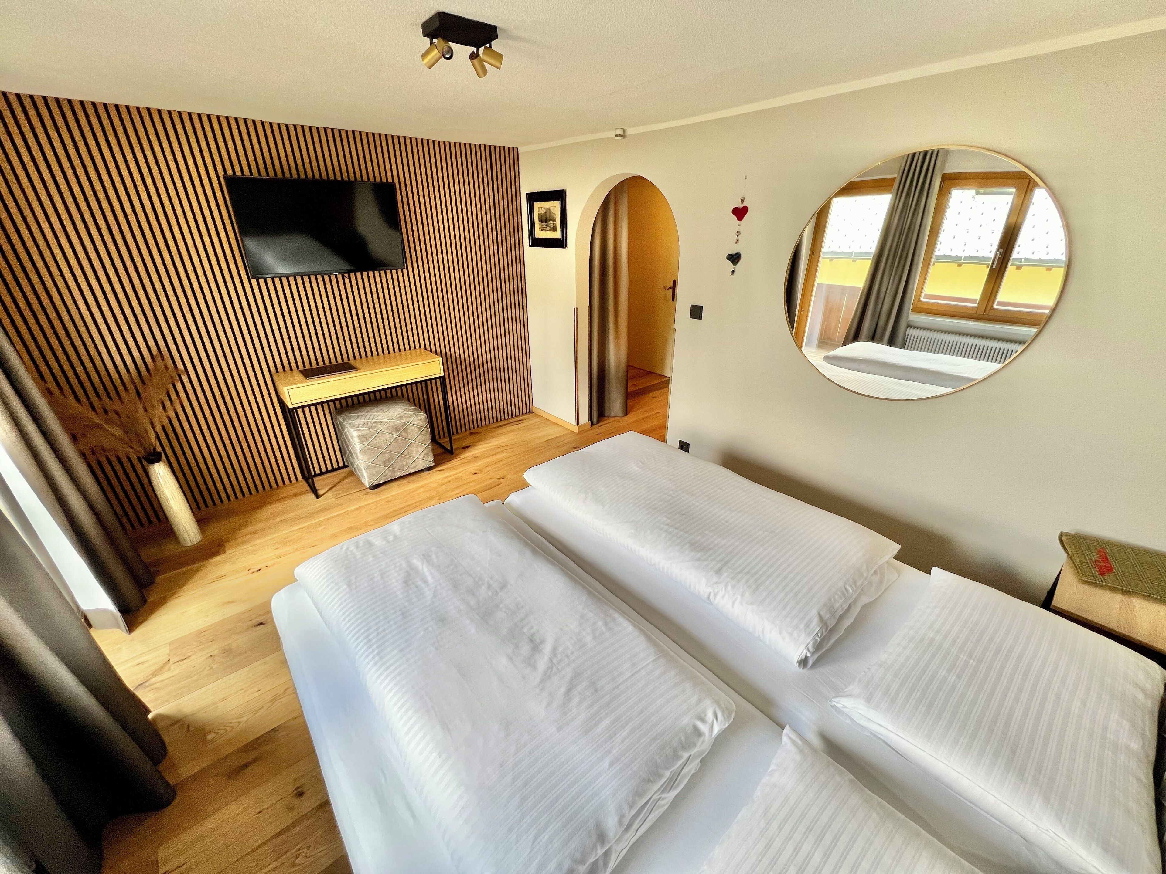 A hotel room with two beds, a desk, a TV, a mirror, and a view of the outdoors.