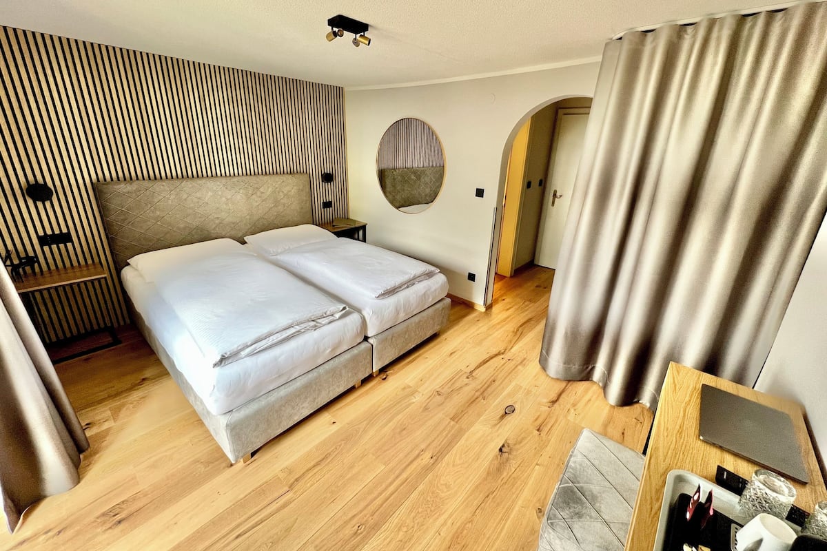 Una habitación de hotel moderna con una cama grande, una mesita de noche, un espejo y suelo de madera.