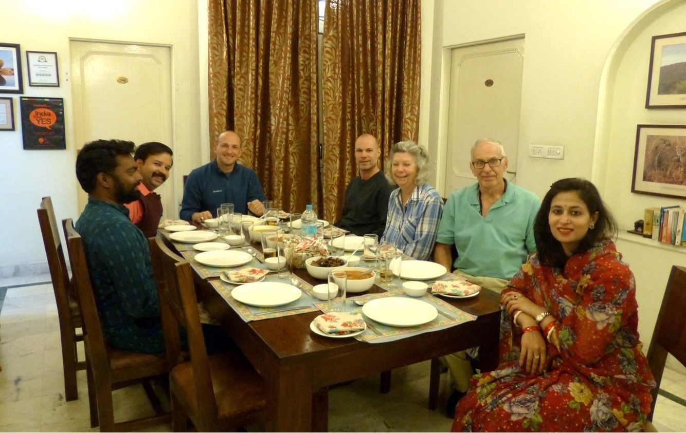 A group of people seated around a wooden dining table with plates, glasses, and bowls.