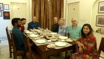 A group of people seated around a wooden dining table with plates, glasses, and bowls.