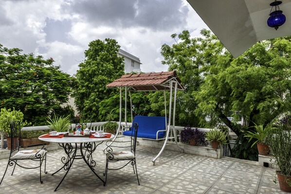 Un patio al aire libre con una mesa redonda, sillas, un sofá azul y una pérgola.