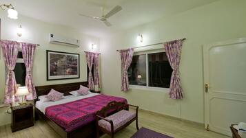 Un dormitorio con cama, mesita de noche, lámpara, ventana con cortinas y un ventilador de techo.